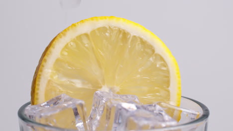 Cold-fresh-sparkling-water-pouring-into-a-glass-with-ice-and-lemon-slices