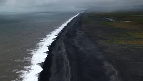 Dyrhólaey-beach-from-above,-well-known-because-of-it's-black-sand,-reaching-the-horizon-on-a-cloudy-day