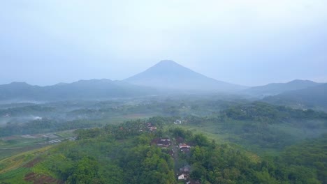 Reveal-drone-shot-of-rural-landscape-in-the-misty-morning-with-huge-mountain-on-the-background