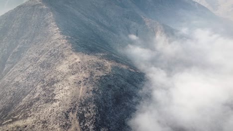 Drohnenaufnahme-Einer-Wolke,-Die-In-Einem-Bergkamm-In-Der-Wüste-Von-Lima,-Peru,-Gefangen-Ist