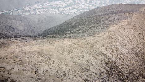 Neigende-Drohnenaufnahme-Von-Wanderern-Auf-Einem-Bergkamm-Neben-Der-Stadt-Lima-Peru-Während-Des-Sonnenaufgangs