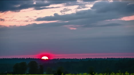 Pink-sunset-as-the-sun-dips-below-the-forest-on-the-horizon-during-a-dramatic-cloudscape---time-lapse