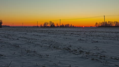 A-golden-dawn-as-the-sunrise-illuminates-a-farmland-field-covered-in-snow---time-lapse