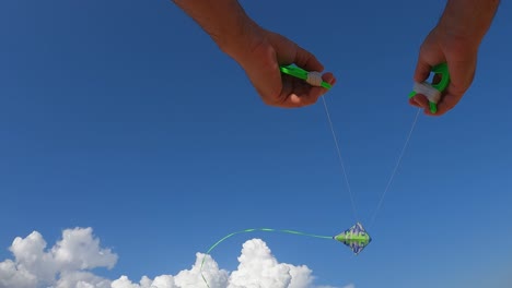 Low-angle-pov-of-male-hands-controlling-flying-green-kite-high-up-in-blue-sky-holding-green-reels