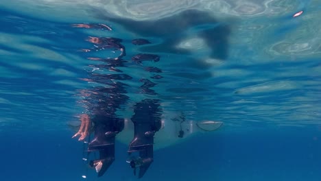 Slow-motion-under-water-footage-of-legs-and-feet-in-sea-water-beneath-surface-hanging-from-speedboat-ladder