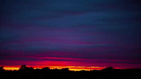 Erstaunlicher-Bunter-Sonnenuntergang-über-Den-Waldbäumen-Mit-Violetten-Und-Roten-Wolken,-Die-Fließen---Zeitraffer