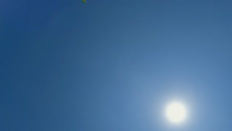 Ungewöhnliche-Perspektive-Des-Fliegenden-Grünen-Spielzeugdrachens-In-Der-Nähe-Der-Strahlenden-Sonne-Am-Klaren-Blauen-Himmel