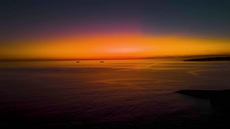 Erstaunlicher-Gelber-Und-Orangefarbener-Himmel-Nach-Sonnenaufgang,-Der-Sich-Auf-Der-Meeresoberfläche-Widerspiegelt,-Mit-Einigen-Booten,-Die-In-Cascais-Segeln