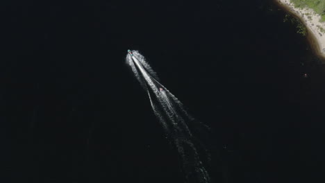 Aerial-wide-view-of-a-ringo-ride-behind-a-fast-jetski-in-deep-dark-water-in-a-river-in-Sweden