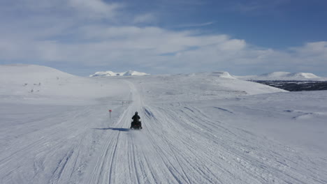 Aerial-slow-motion-footage-of-a-man-on-a-snowmobile-speeding-past-the-camera-in-winter-landscape-in-Sweden