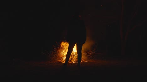 Person-Walking-Towards-Campfire-At-Night-Time,-Silhouette-In-Darkness
