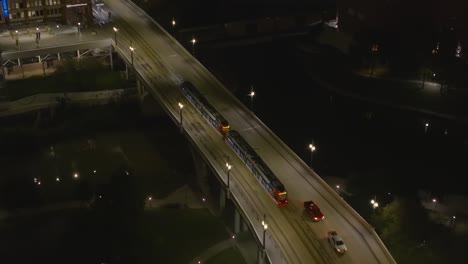 Aerial-view-following-a-tram-passing-a-bridge-in-downtown-Houston,-night-in-Texas,-USA