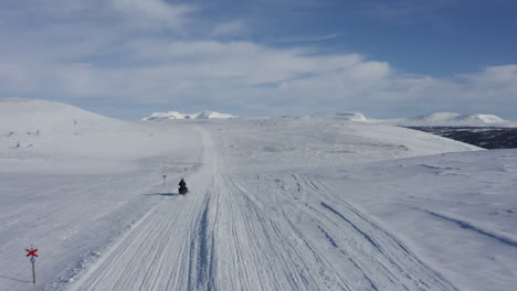 Aerial-footage-of-a-man-on-a-snowmobile-speeding-past-the-camera-in-winter-landscape-in-Sweden