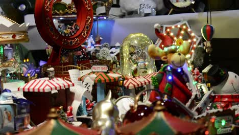 A-person-choosing-with-his-hand-christmas-toys,-snowball-and-carousel-with-multi-colored-lights-in-a-christmas-market