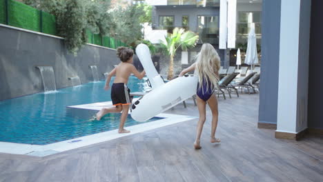 girl-and-boy-run-by-the-pool-with-pool-toy-in-their-hands