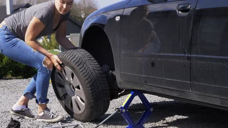 Young-casual-female-changing-deflated-car-tyre-at-side-of-road