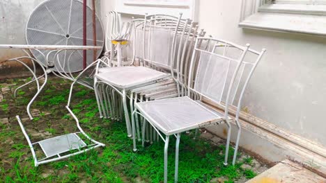 Stacks-of-old-white-outdoor-iron-chair-in-front-of-a-house-as-trash