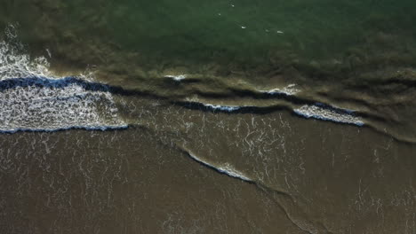 God's-eye-aerial-top-down-view-of-ocean-waves-on-dark-sand-of-California