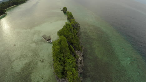 Aerial-of-long-tropical-lava-rock-island-with-small-ship-wreck-transition-to-strait-down-view