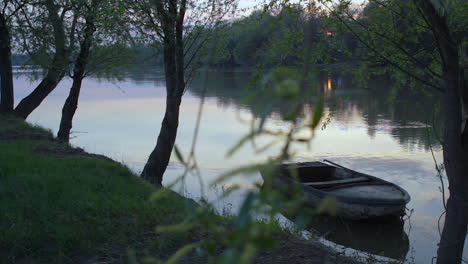 Weite-Aufnahme-Einer-Impressionistischen-Stimmung-Grüner-Waldlandschaft-Mit-Rostigem-Boot,-Das-Auf-Dem-Ruhig-Wehenden-Ungarischen-Theißsee-Im-Sommer-Orange-Sonnenuntergang-Schwimmt