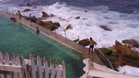 The-beautiful-Bronte-Beach-in-Australia-with-a-pool-overlooking-the-waves-crashing-and-splashing-on-large-rocks-by-the-shore---Slow-motion