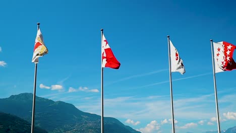 Four-Swiss-flags-fly-against-blue-sky-blowing-in-wind-slow-motion