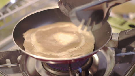Caucasian-right-hand-flips-pancake-in-skillet-with-metal-tong,-slowmo-close-up
