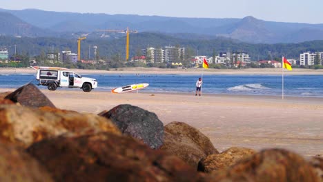 Man-Putting-A-Lifeguard-On-Duty-Flags-On-The-Sandy-Beach-Shore---Lifeguard-Vehicle-Parked-At-Snapper-Rocks---Gold-Coast,-Queensland,-Australia