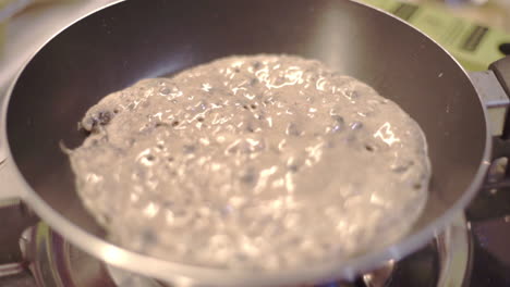 One-round-pancake-bubbling-and-cooking-in-a-hot-skillet,-slowmo-close-up