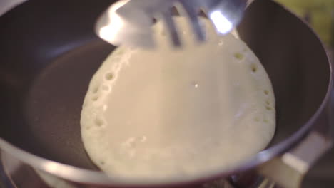 Foamy-pancake-being-flipped-in-a-frying-pan-closeup
