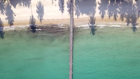 Luftbild-Von-Oben-Nach-Unten-Auf-Den-Wunderschönen-Weißen-Sandstrand-Mit-Palmen,-Die-In-Richtung-Steg-Fliegen