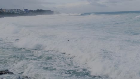 Männer-Schwimmen-Am-Strand-Von-Bronte-Mit-Riesigen-Wellen,-Die-An-Die-Küste-Rollen---Sydney,-NSW,-Australien---Weitschuss
