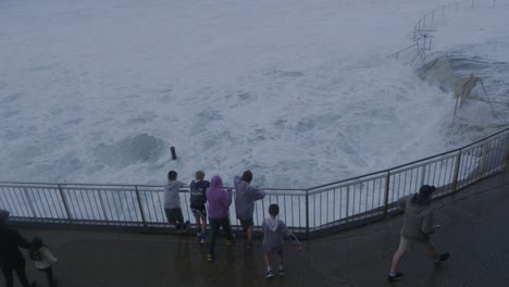 Kids-Leaning-On-The-Metal-Railings-Watching-The-Rough-Waves-At-The-Bronte-Beach---Water-Overflowing-At-Bronte-Rock-Pool-During-Storm---Sydney,-NSW,-Australia