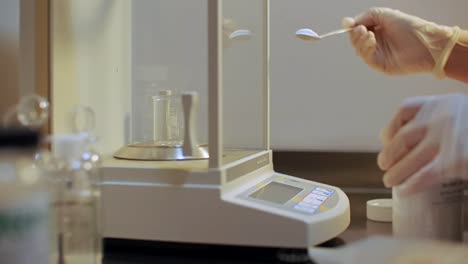 gloved-hands-in-the-lab-pour-powder-into-the-beaker-on-the-scale