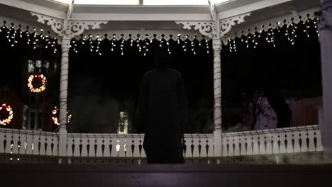 Tilt-up-WIDE-SHOT-of-someone-in-a-Grim-Reaper-costume-in-front-of-Christmas-lights
