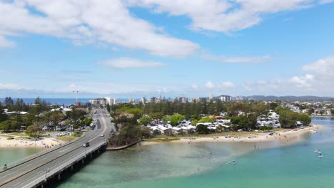 The-Tallebudgera-Creek-Bridge-With-Vehicles-Passing-By---Tourists-Enjoying-At-The-Beautiful-Beach-In-Burleigh-Heads,-QLD---ascending-drone-shot