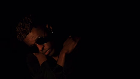 Black-man-with-bleached-hair-and-sunglasses-hugging-himself-in-dark