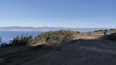 Motorrad-Abenteuerfahrer-Fährt-Auf-Einer-Schotterstraße-Mit-Blick-Auf-Das-Meer-Und-Die-Stadt-In-Baja-California-Mexiko-Vorbei