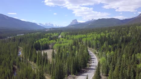 Motorcycle-driving-by-in-Dreamlike-Snow-Covered-Mountain-Tops-and-Green-Spruce-Forest-area-in-Canada,-Aerial