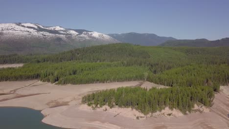 Large-Evergreen-Forest-next-to-Snow-Covered-Mountain-Peek-and-Lake-in-Canada,-Aerial-Reveal