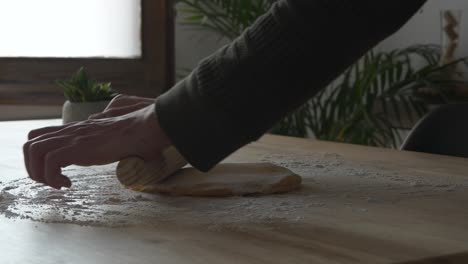 Man's-hands-working-on-spreading-pasta-dough-with-a-roller-on-wooden-table-with-flour-on-it