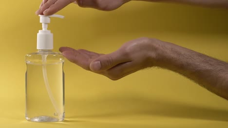 Rubbing-hands-with-alcoholic-based-sanitizer-against-yellow-background