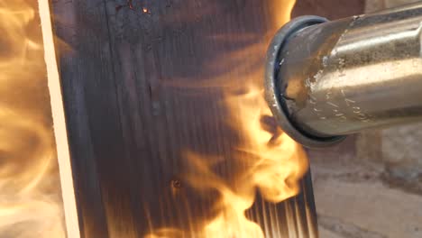 Gas-blowtorch-burning-pine-wood-plank,-close-up