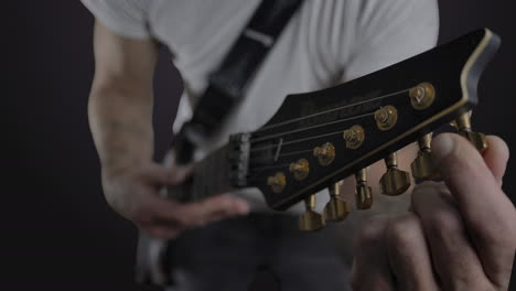 Male-with-tattoos-tuning-an-electric-guitar-in-slow-motion-with-headstock-in-foreground-and-in-focus