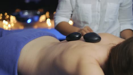 In-the-massage-room,-the-masseuse-is-putting-hot-stones-on-the-woman's-back