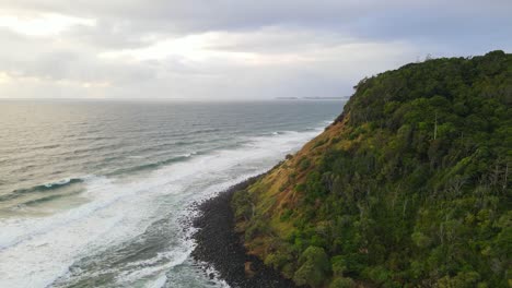 White-Waves-Crashing-At-The-Feet-Of-Forested-Burleigh-Headland-In-Gold-Coast,-Queensland-On-A-Cloudy-Sunset