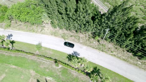 Aerial-shot-of-black-car-riding-through-empty-rural-road