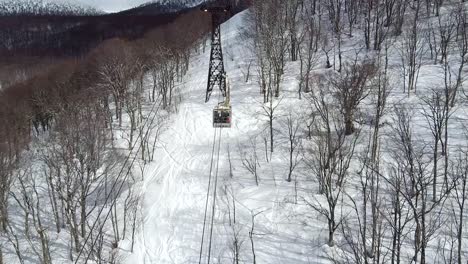 Aerial---drone-shot-of-ski-gondola-travelling-up-snowy-mountain
