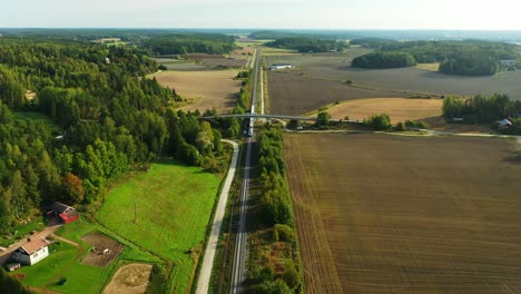 High-altitude-tracking-aerial-drone-view-of-high-speed-passenger-train-traveling-on-long-straight-railroad-with-fields-and-forests-on-both-sides