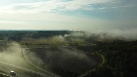 Backwards-moving-aerial-view-of-morning-fog-floating-over-a-4-lane-highway-with-cars-and-trucks